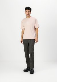 Light pink cotton t-shirt with a chest logo, paired with textured gray trousers and black shoes. Simple, relaxed fit with short sleeves.