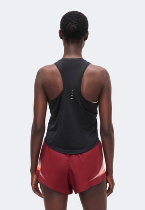 Persona vista da dietro che indossa un top sportivo nero senza maniche e pantaloncini da corsa rossi con dettagli bianchi.