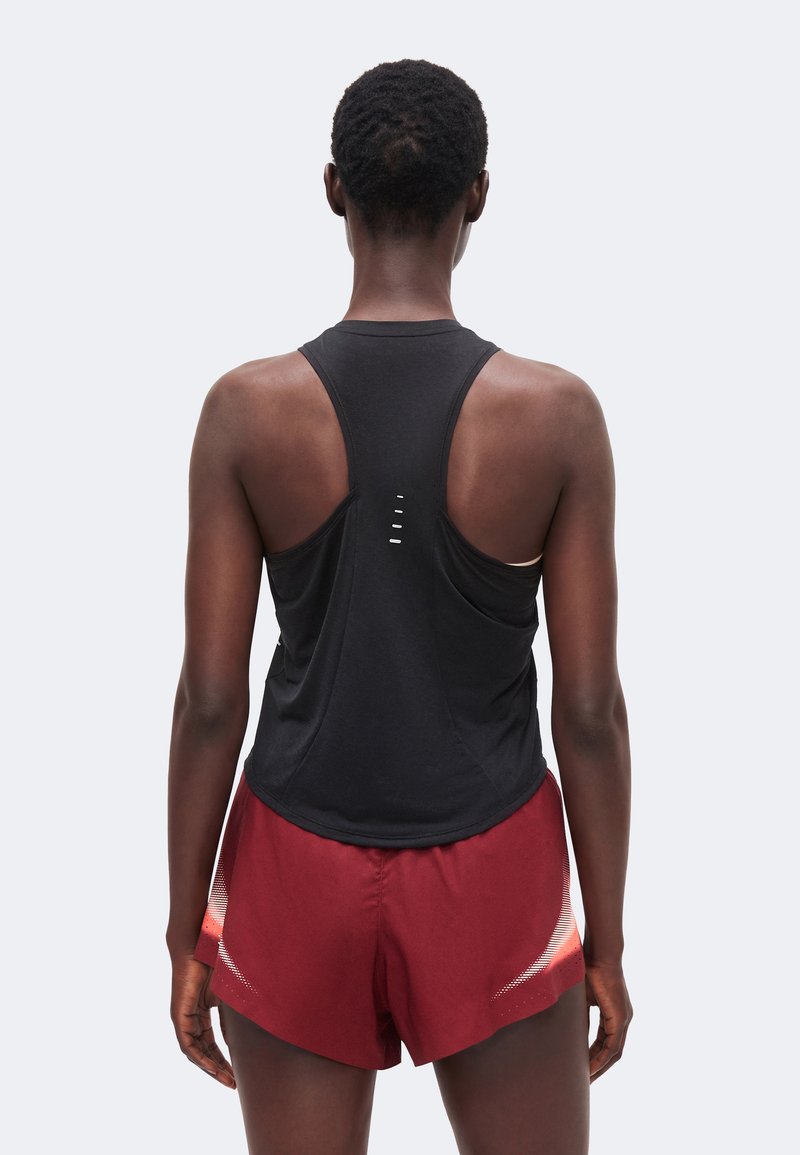 Personne vue de dos portant un haut de sport noir sans manches et un short de course rouge avec des détails blancs.