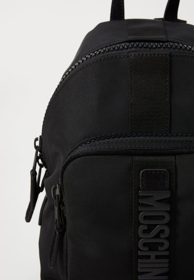 Rucsac negru din nailon, cu o textură netedă, fermoare duble și un logo proeminent "MOSCHINO" pe curea frontală. Design compact și elegant.