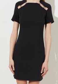 Schwarzes, tailliertes Kleid mit kurzen Ärmeln, Ausschnitten an den Schultern und runden Metallakzenten. Glattes, strukturiertes Material.