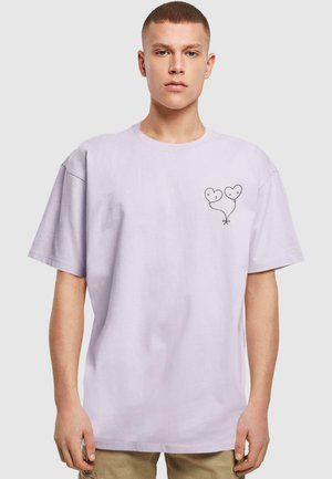 Lavenderfarbenes Oversized-T-Shirt aus Baumwolle mit einem kleinen schwarzen Herzluftballon-Graphic auf der linken Brustseite. Kurze Ärmel, Rundhalsausschnitt.
