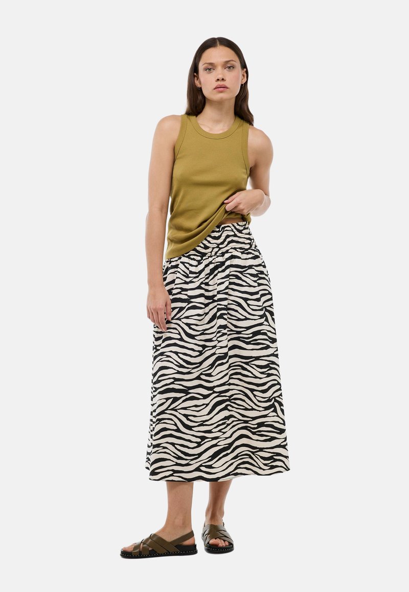 Débardeur côtelé olive, jupe maxi rayée noir et blanc à motif zèbre, et sandales à glisser vert foncé. La jupe présente une taille élastique.