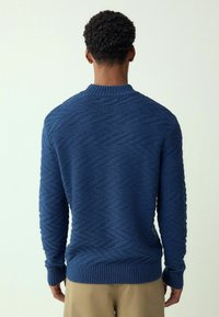 Niebieski sweter dziany z wzorem w romby, z prążkowanymi mankietami i dołem, okrągłym dekoltem oraz teksturowaną tkaniną. Pokazany widok z tyłu.