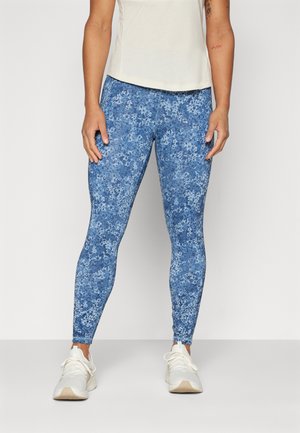 Blå blomstrete leggins laget av elastisk stoff, med et lyst blomsterdesign, kombinert med en lys topp og hvite joggesko.