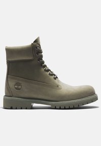 Bottine en cuir vert olive pour homme à lacets, col matelassé et semelle texturée, avec un logo d'arbre sur le côté.