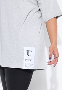 Camiseta de gran tamaño gris claro, hecha de tejido suave, con mangas cortas y una etiqueta blanca con texto negro en el lateral.