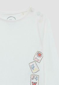 Witte babyshirt met drie kleurrijke stempelachtige ontwerpen met zon, krab, ster en zeethema's, en twee drukknoopjes op de schouders.