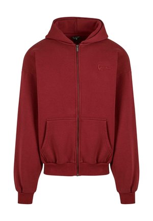 Red zip-up hoodie made of soft fabric, featuring a large hood, front pockets, ribbed cuffs, and a discreet logo on the chest.