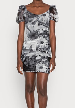 Mujer con un vestido corto y ajustado de flores con mangas abullonadas en tonos blanco y negro, con grandes patrones de flores y tela fruncida.