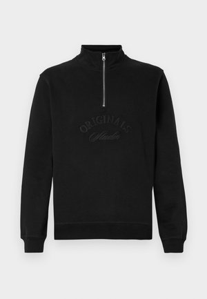 Černá zipová mikina vyrobená z měkké tkaniny, s vysokým límcem, dlouhými rukávy a vyraženým detailem "ORIGINALS Studio" na přední straně.