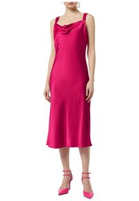 Sukienka bez rękawów z dekoltem typu cowl w intensywnym różowym odcieniu satyny, o płynnej sylwetce, dopełniona pasującymi szpilkami z paskami na kostce.