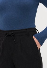 Suéter azul con textura de canalé y mangas largas, combinado con pantalones de pana negros con cintura ajustable y bolsillos.