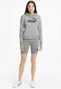 Felpa con cappuccio grigia con logo "PUMA" nero, abbinata a pantaloni bike grigi con un logo simile. Entrambi sono realizzati in morbido tessuto jersey.