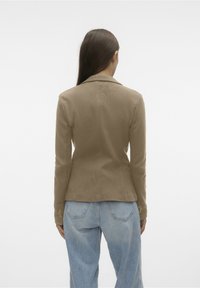Light brown blazer with a textured finish, fitted silhouette, and classic lapels. Features buttoned cuffs and is worn over blue denim jeans.
