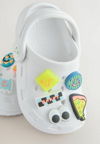 Sabots blancs ornés de charms colorés et ludiques, incluant des visages souriants et une part de pizza, mettant en avant un design amusant et personnalisable.