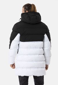 Puffy Jacke mit einem Schwarz-Weiß-Farbblockdesign, ausgestattet mit einer Kapuze und einem horizontalen Steppmuster. Glatte Textur und funktionale Details.