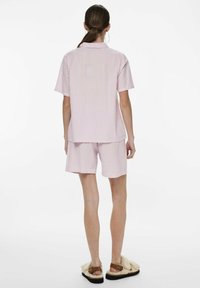 Set di camicia a manica corta e pantaloni corti a righe rosa e bianche, caratterizzato da una vestibilità rilassata e una texture morbida. Indossato con sandali in peluche.
