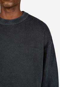 Adīts tumši pelēks džemperis ar ribotu apkakli, kas piedāvā smalku tūko logo uz krūšu un brīvu piegriezumu.