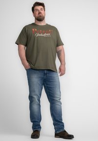 Camiseta verde oliva con el logo "PetroD Industries", combinada con jeans de mezclilla azul claro y zapatos marrones oscuros. Diseño simple y casual.