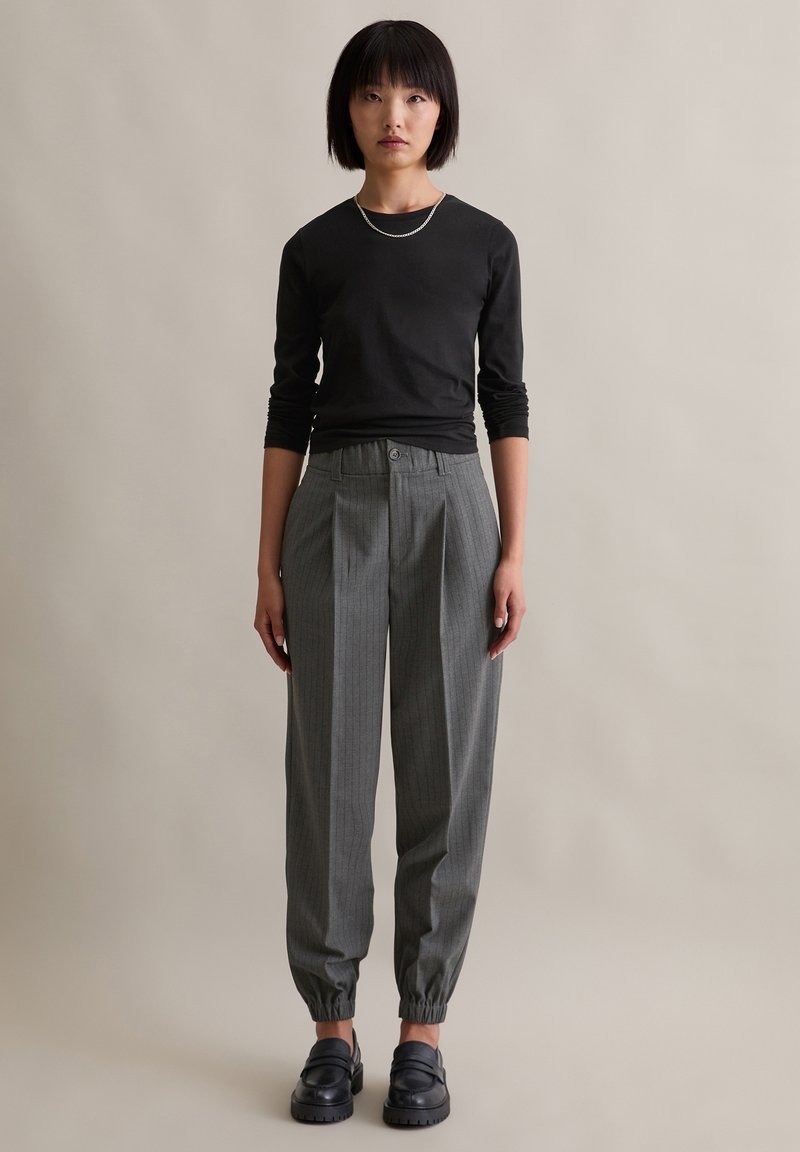 Czarna koszula z długim rękawem, szare spodnie w prążek z elastycznym mankietem i czarne klapki. Prosta srebrna bransoletka jako akcent.