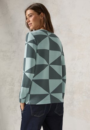 Svetr ve světle modré a tmavě zelené barvě s geometrickým vzorem. Má dlouhé rukávy, ribbovanou texturu a uvolněný střih.