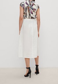 Falda de lino blanca con un corte a media longitud y una textura sutil. Combinada con una blusa de estampado multicolor y sandalias de tacón negras.