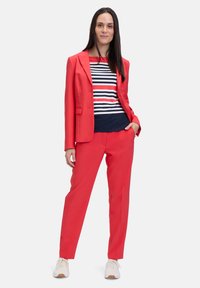 Czerwony garnitur z marynarką i spodniami w połączeniu z koszulą w granatowe paski. Gładki materiał z dopasowanym krojem. Białe trampki dopełniają outfit.