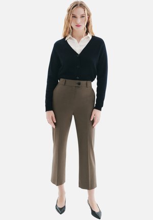 Cardigan marine sur une chemise blanche, associé à un pantalon marron taille haute. Présente un design ajusté et des talons noirs pointus.