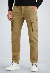Pantalons cargo beiges avec plusieurs poches, coupe droite, fabriqués en tissu durable, associés à des baskets blanches et un haut noir.