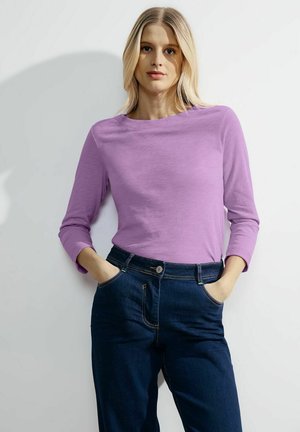 Maglietta a maniche lunghe di colore viola realizzata in tessuto morbido, abbinata a jeans blu scuro con chiusura a bottone e tasche laterali.