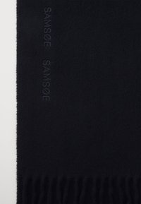 Bufanda de lana negra con bordes deshilachados, que presenta un logotipo grabado "SAMSØE" a lo largo de un lado. Textura suave con un color uniforme y un diseño minimalista.