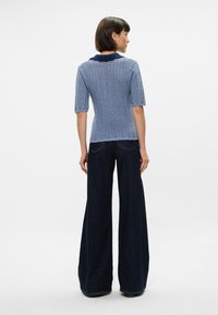 Πλεκτό μπλε πουλόβερ με κοντά μανίκια, με υφή κυματοειδούς σχεδίου και σκούρο γιακά, συνδυασμένο με σκούρες καμπάνα τζιν.