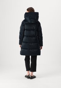 Palton lung căptușit în navy închis cu un model în carouri, dotat cu glugă și talie strânsă, purtat cu pantaloni scurți negri și pantofi.