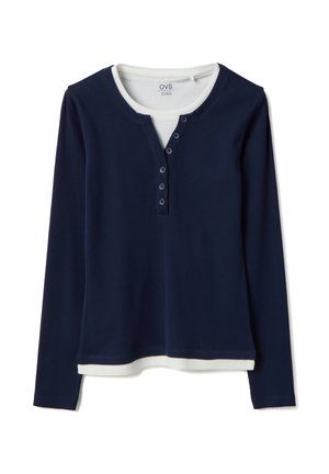 Camisa henley de manga larga en azul marino con cinco botones y cuello y dobladillo blanco acanalados, usada sobre una camiseta blanca.