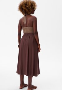Bruine midi-jurk met een getailleerde, strapless corsage en een uitlopende rok. De corsage heeft een textuurstof en de rok heeft plooien bij de taille.