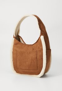 Sac à épaule en suede marron avec un bord en fausse fourrure crème et une grande poche avant, posé sur un fond blanc uni.