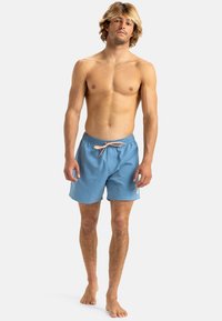Blue swim shorts with an elastic waistband and front drawstring. Lightweight material, above knee length, featuring a small logo tag.