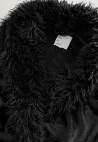 Juodas aksominis chalatas su pailgintu pūkuotu apykakle. Ant audinio etiketės parašyta „laikas svajoti“. Minkšta tekstūra su lygiu vidiniu pamušalu.