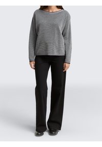 Grauer strukturierter Pullover mit weitem Ausschnitt, kombiniert mit schwarzen Weithosen und schwarzen Schuhen, auf einem schlichten hellen Hintergrund präsentiert.