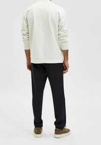 Ljust sweatshirt med ribbade muddar, tillsammans med mörka, löst sittande sweatpants och bruna sneakers. Vy från baksidan.