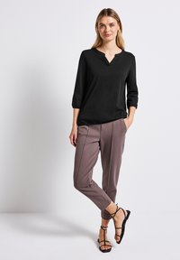 Zwarte, lichte blouse met een V-hals en driekwartmouwen, gecombineerd met taupe tapered broeken met zijnaaddetails en zwarte gekruiste sandalen.