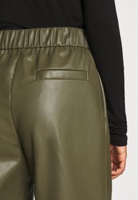 I pantaloni in ecopelle verde oliva presentano una vita elastica e una singola tasca sul retro, con una texture liscia e una vestibilità sartoriale.