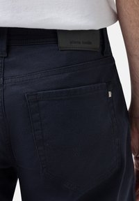 Mörk marinblå denimjeans med en synlig bakficka med dekorativ söm, en märkesskinnlapp och en mjuk textur.