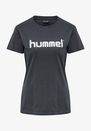 Camiseta de algodón negra con mangas cortas y cuello redondo, adornada con un gran logo blanco de "hummel" impreso en la parte delantera.