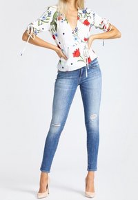 Bluse mit floralem Druck in Weiß, mit tiefem V-Ausschnitt und gerafften Ärmeln, kombiniert mit hellblauen, distressten Skinny-Jeans und nudefarbenen High Heels.