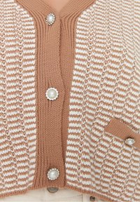 Pletený cardigan s pruhovaným designem v hnědé a krémové barvě, zdobený perlovo podobnými knoflíky a detaily kapsy.