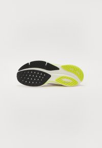 Schoenen met een gestructureerde zwarte rubberen buitenzool, met heldergroene accenten en een grijze basis. Opvallende driehoekige grippatronen aanwezig.