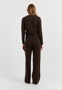 Bruine gebreide twee-delige outfit met een crew neck trui en wijde pijpen met een achterzak. Zachte textuur en een comfortabele pasvorm.