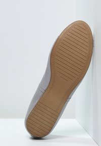 Zapato de cuero gris con parte superior texturizada y suela de goma color beige claro que muestra patrones de relieve, exhibido en un ángulo sobre un fondo blanco.